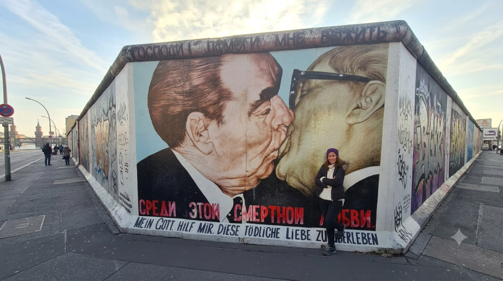 A traveler taking a photo of the famous Fraternal Kiss mural on the Berlin Wall's East Side Gallery - Berlin Travel Guide