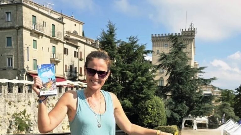 Smiling tourist woman holding a travel guide brochure in San Marino historical city center