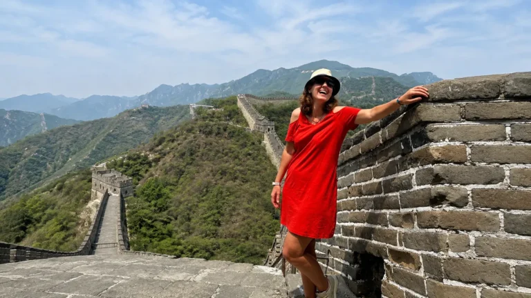 traveler in a red dress smiling on the Great Wall of China, mountain ridgeline behind