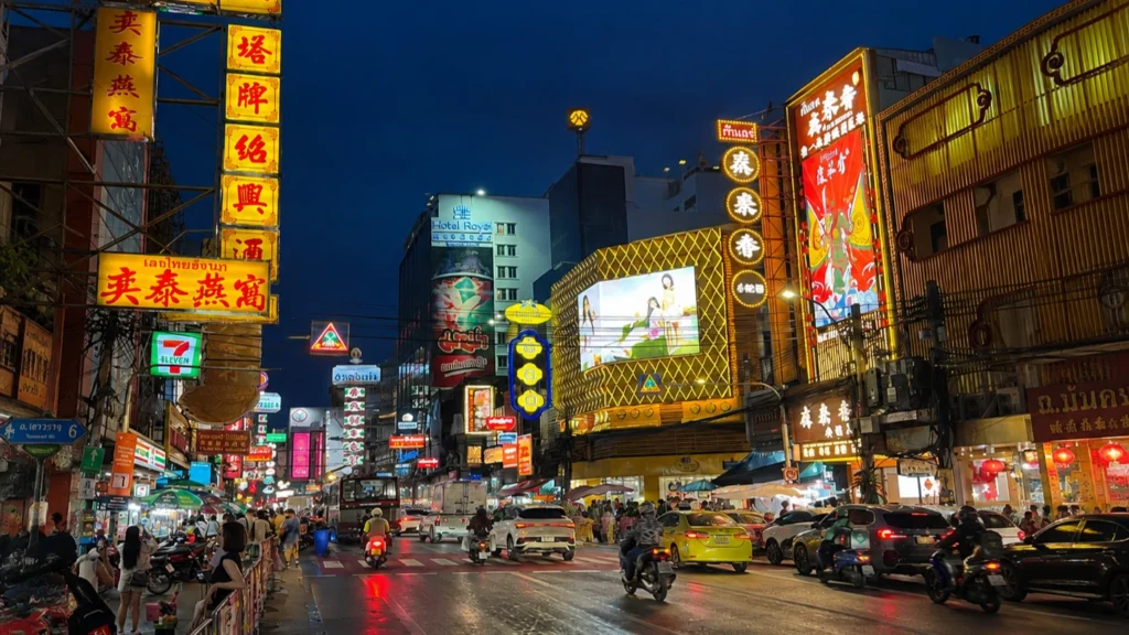 Bangkok Chinatown (Yaowarat Road) at night with colorful neon signs, busy traffic, and vibrant street atmosphere in Thailand.