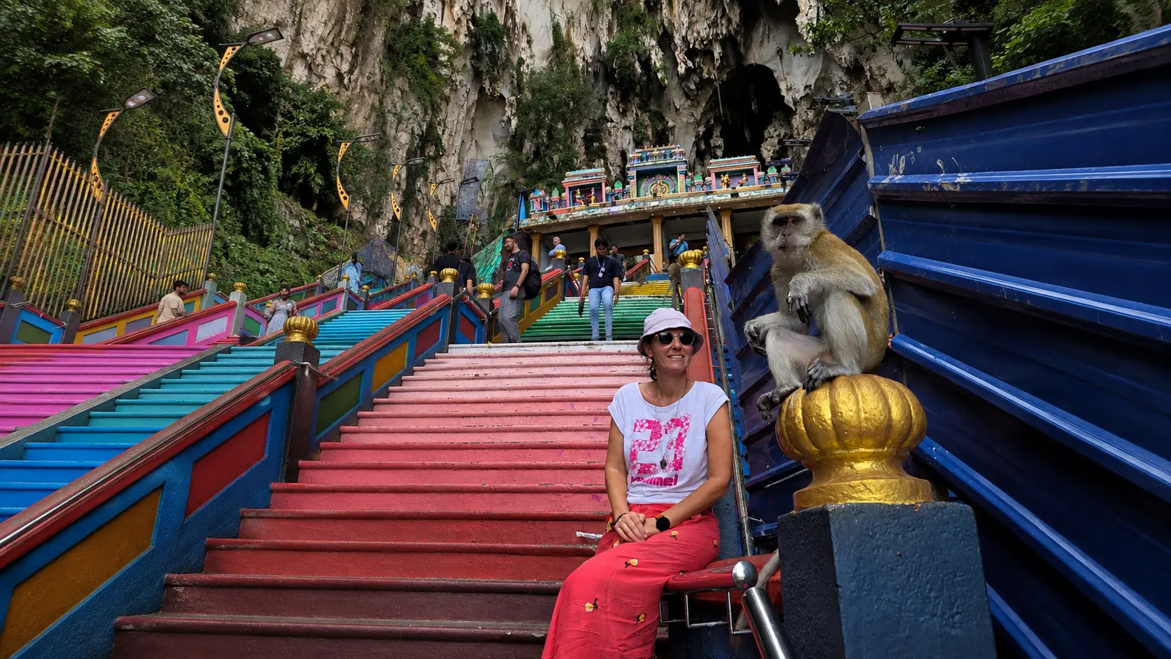 traveler on the colorful steps of Batu Caves with a macaque nearby