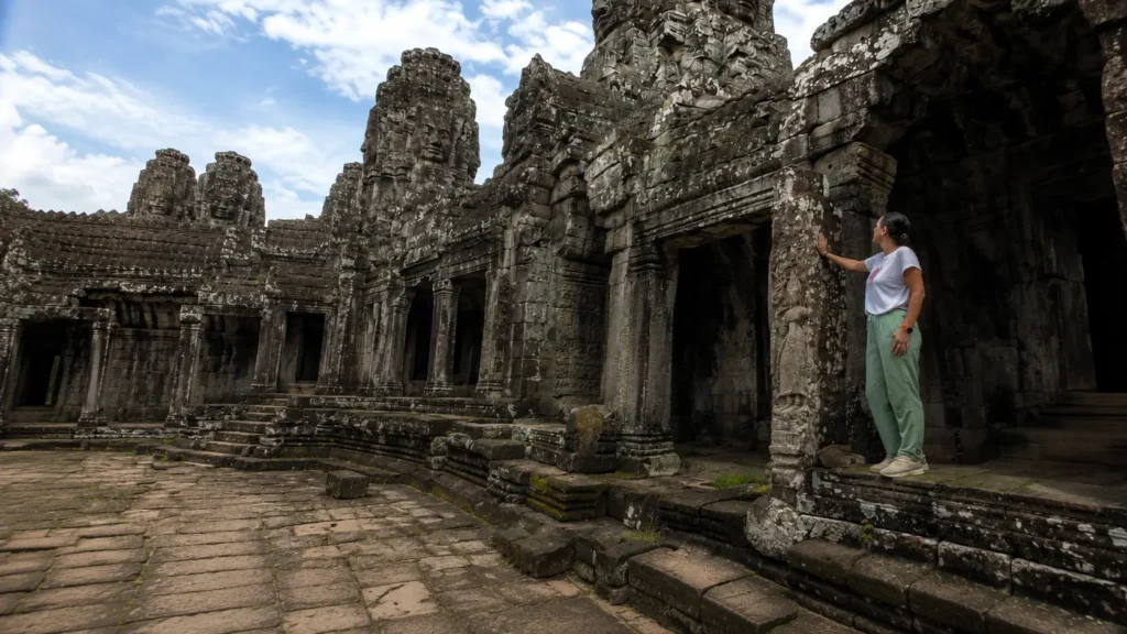 Traveler exploring the carved stone galleries and face towers of Bayon Temple, Angkor, Siem Reap
