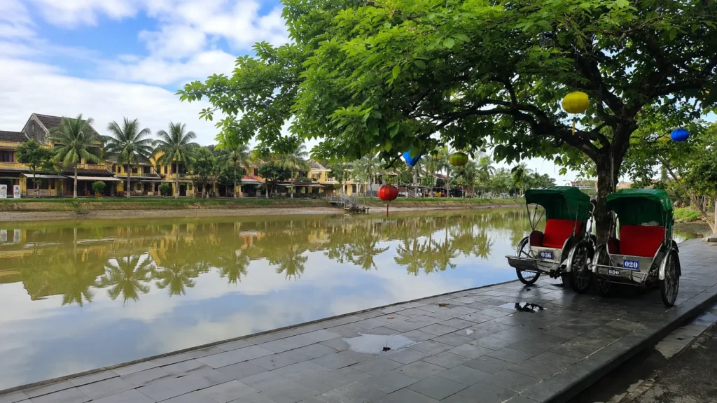 cyclo rickshaws parked along the riverside in Hoi An with the Old Town in the background