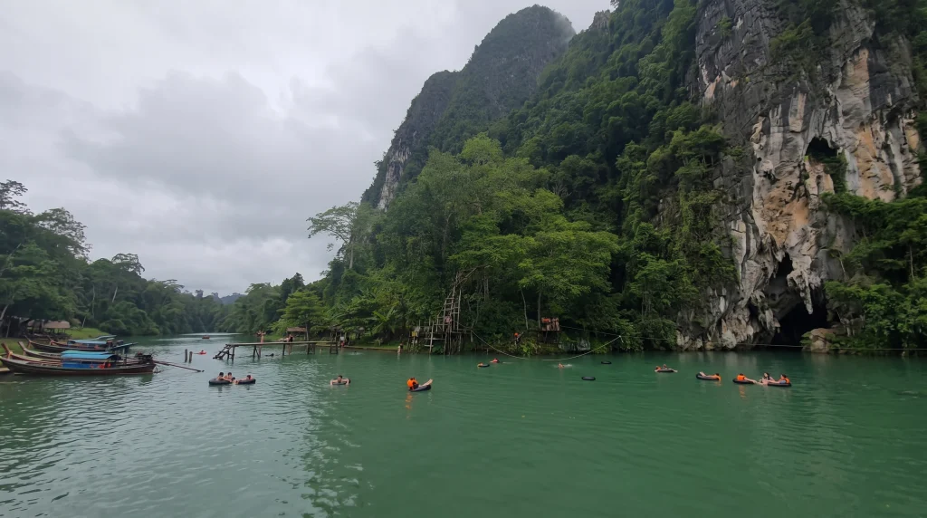 Tourists floating on tubes in a lagoon near limestone cliffs and a cave in Vang Vieng