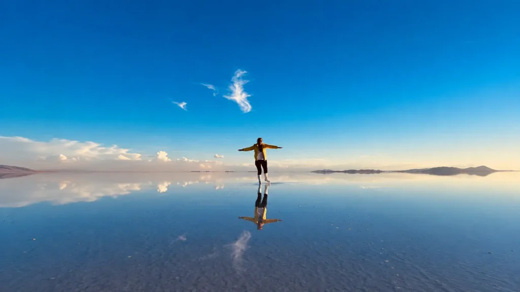 standing on the Salar de Uyuni mirror with arms spread, blue sky