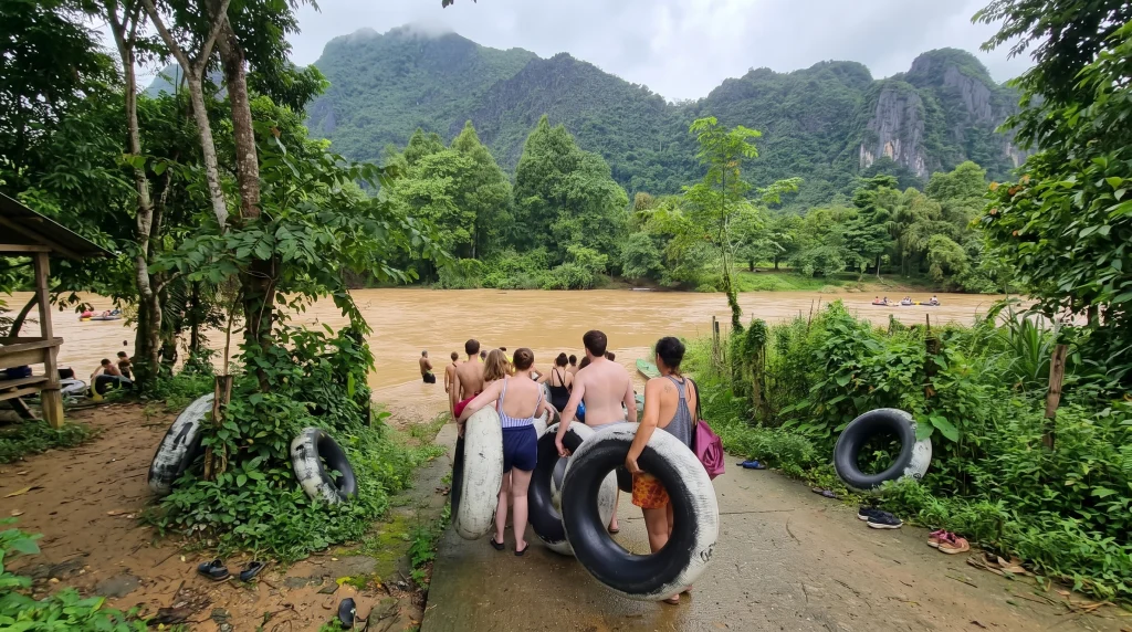 Travelers carrying inner tubes before tubing on the Nam Song River with karst mountains behind them