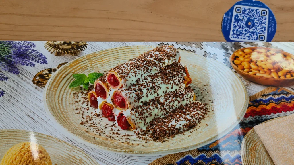 Cucuma lui Guguță Moldovan pastry roll dusted with cocoa powder, topped with raspberries, served on white ceramic plate with traditional textile