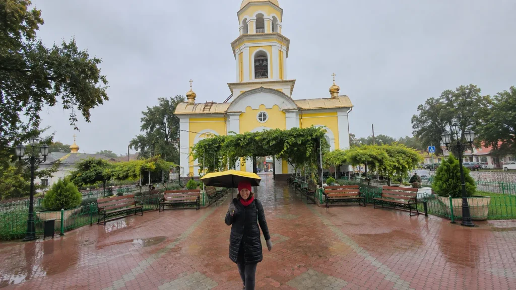 Bright yellow Orthodox church with white trim and golden domes in Gagauzia, Moldova, wet ground reflecting rainy autumn weather