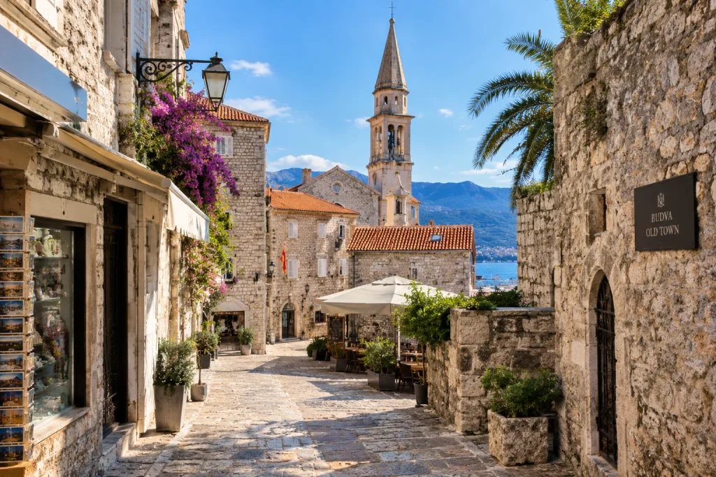 Cobbled stone lane in Budva Old Town with a bell tower, flowering vines and a cafe terrace