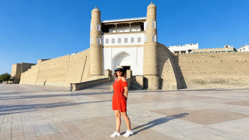 Visitor in a red dress in front of the Ark Fortress gate and towers in Bukhara