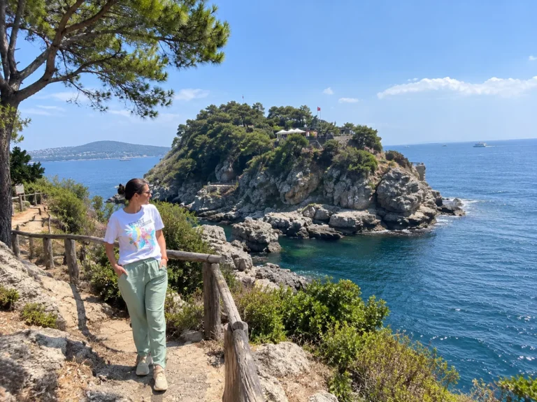 Burgazada travel guide: woman on a coastal path looking at the rocky headland with the Kalpazankaya restaurant above the sea