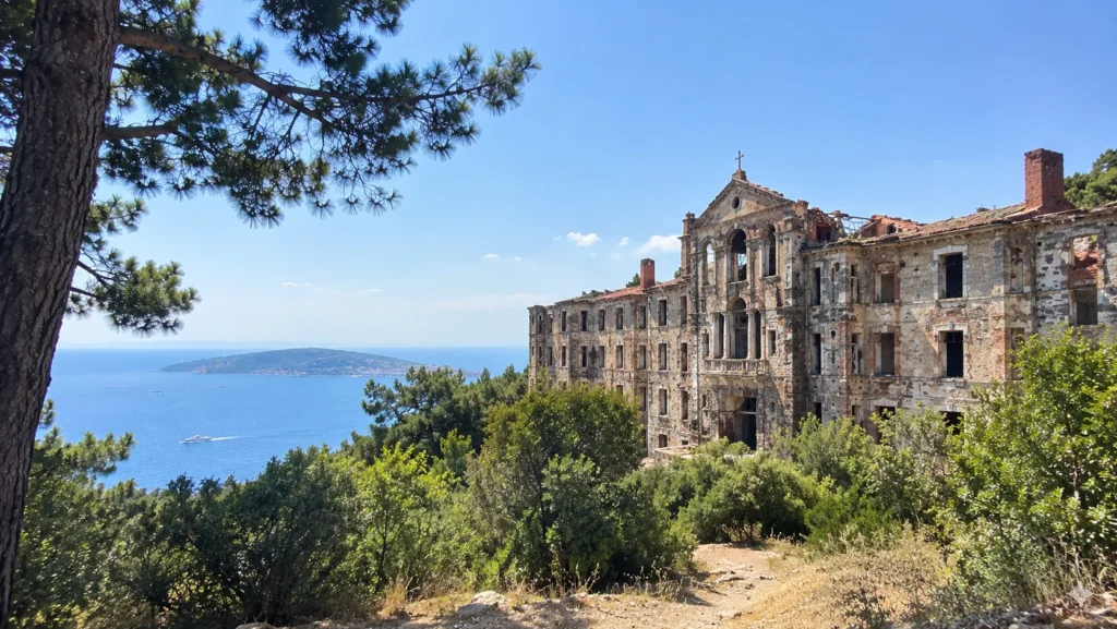 Ruined wooden Prinkipo Greek Orphanage building seen through pine trees on Büyükada with the sea behind