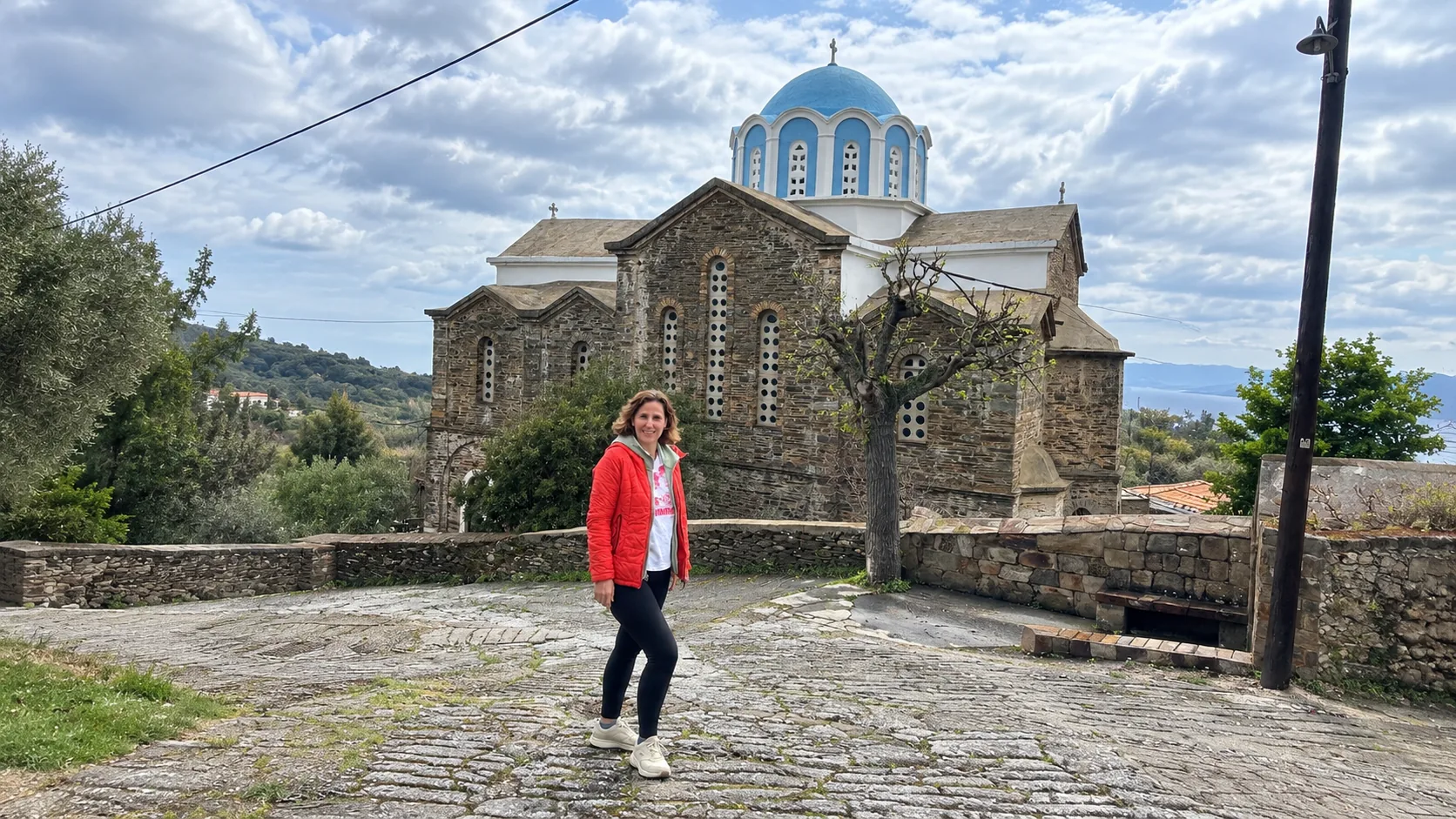 Ikaria travel guide: traveler in front of a blue-domed stone church on a cobbled village square