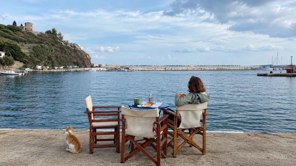 Cafe table by the harbor with a cat watching the water on Ikaria island