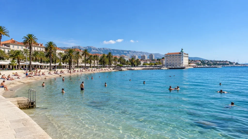Swimmers in clear shallow water at Bačvice Beach in Split with palm trees and the seafront behind